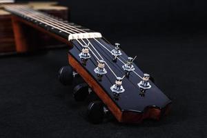 Stimmwirbel auf hölzernem Maschinenkopf von sechs Saiten Akustikgitarrenhals auf schwarzem Hintergrund foto