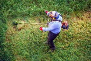 draufsicht rasenmäher mann arbeiter schneiden trockenes gras mit rasenmäher. foto