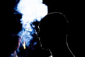 Silhouette eines Mannes, der die Zigarette im Dunkeln anzündet