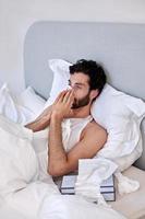 Ein kranker und depressiver Mann mit Papiertaschentüchern im Bett