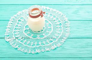 Mittagszeit mit Krug Milch und kariertem Band auf blauem Holzhintergrund. Spitze Tischdecke. selektiver Fokus foto