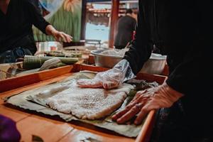 fokus alte frau mit traditionellem vietnamesischem kleid ao ba ba machen, verpacken tet kuchen, das vietnamesische mondneujahr tet essen im freien von händen. foto