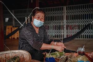 fokus alte frau mit traditionellem vietnamesischem kleid ao ba ba machen, verpacken tet kuchen, das vietnamesische mondneujahr tet essen im freien von händen. foto