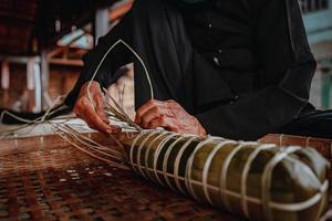 fokus alte frau mit traditionellem vietnamesischem kleid ao ba ba machen, verpacken tet kuchen, das vietnamesische mondneujahr tet essen im freien von händen. foto