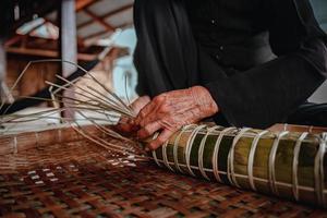 fokus alte frau mit traditionellem vietnamesischem kleid ao ba ba machen, verpacken tet kuchen, das vietnamesische mondneujahr tet essen im freien von händen. foto