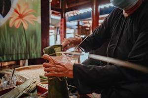 fokus alte frau mit traditionellem vietnamesischem kleid ao ba ba machen, verpacken tet kuchen, das vietnamesische mondneujahr tet essen im freien von händen. foto