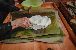 fokus alte frau mit traditionellem vietnamesischem kleid ao ba ba machen, verpacken tet kuchen, das vietnamesische mondneujahr tet essen im freien von händen. foto