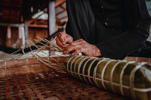 fokus alte frau mit traditionellem vietnamesischem kleid ao ba ba machen, verpacken tet kuchen, das vietnamesische mondneujahr tet essen im freien von händen. foto