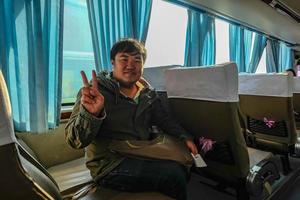 asiatischer dicker mann, der den mantel trägt und zwei finger aufwirft, während er im bus sitzt, wenn er im china reist foto