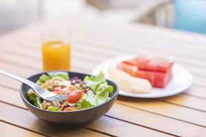 Frühstück. Gemüsesalat, Früchte wie Wassermelone, Papaya, Melone, Maracuja, Orangensaft und Kaffee. platziert auf einem grauen Tischset foto