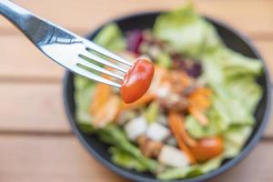 Verwenden Sie eine Gabel, einen Tomatenspieß im Vordergrund und einen Salat im Hintergrund. Frühstückssalat mit sautiertem Gemüse auf einem Holztisch foto