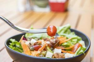 Verwenden Sie eine Gabel, einen Tomatenspieß im Vordergrund und einen Salat im Hintergrund. Frühstückssalat mit sautiertem Gemüse auf einem Holztisch foto