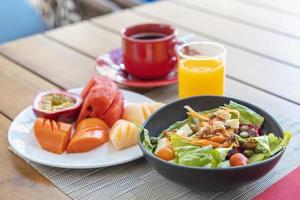 Frühstück. Gemüsesalat, Früchte wie Wassermelone, Papaya, Melone, Maracuja, Orangensaft und Kaffee. platziert auf einem grauen Tischset. foto