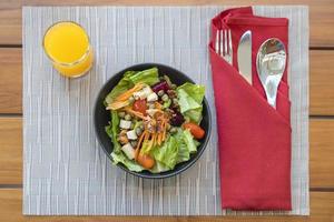 Frühstückssalat mit sautiertem Gemüse und Orangensaft und mit einem Löffel, Fixierung, Messer ruht auf einem grauen Tischset foto