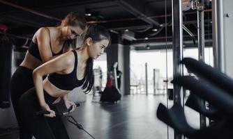 sportliches mädchen, das mit hilfe ihres persönlichen trainers im fitnessstudio gewichtsübungen macht. foto