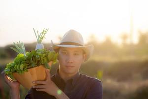 porträt junger asiatischer mann, der die ernte lächelt und frischen bio-gemüsegarten im korb in der hydrokulturfarm, in der landwirtschaft und im anbau für gesunde ernährung und geschäftskonzept aufnimmt. foto