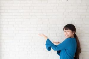 schöne junge asiatische frau, die glücklich steht und lächelt und etwas präsentiert und zukunft oder planung mit nachricht von ihnen auf zementbetonhintergrund, lebensstilkonzept zeigt. foto