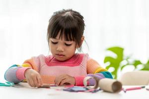 porträt eines kleinen asiatischen mädchens, das ein papier in aktivitäten im diy-unterricht in der schule schneidet. schere schneidet papier. foto