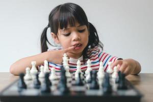 asiatisches kleines mädchen, das zu hause schach spielt. ein schachspiel foto