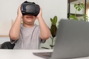 asiatischer kleiner junge mit vr-brille, der zu hause naturwissenschaften studiert, neugieriger student trägt ein virtual-reality-headset, um naturwissenschaften zu hause online zu studieren, futuristischer lebensstil lernen foto