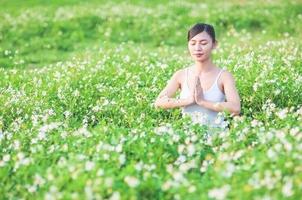 junge dame, die yogaübungen auf der grünen wiese mit kleinen weißen blumen im freienbereich macht, die ruhig friedlich im meditationsgeist zeigen - leute üben yoga für meditations- und übungskonzept foto