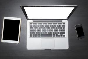 Draufsicht auf Laptop mit Tablet und Smartphone auf schwarzem Schreibtischhintergrund aus Holz. foto