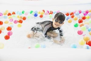 Junge, der mit buntem Ball im kleinen Swimmingpoolspielzeug spielt - fröhlicher Junge im Wasserpool-Spielzeugkonzept foto