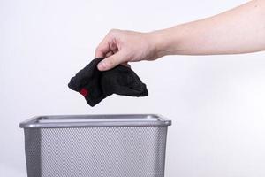Ein Mann wirft eine alte Socke mit der Hand vor weißem Hintergrund in einen Mülleimer. foto