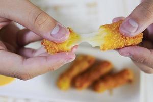 Die Hand hält einen Stretch-Käseball, der bereit ist, mit weich fokussierten Pommes Frites auf blauem Tischhintergrund gegessen zu werden foto