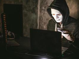 Computerhacker - Mann im Kapuzenshirt mit Maske, der Daten vom Laptop stiehlt foto