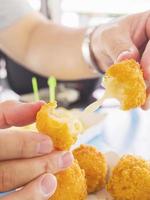 Die Hand hält einen Stretch-Käseball, der bereit ist, mit weich fokussierten Pommes Frites auf blauem Tischhintergrund gegessen zu werden foto