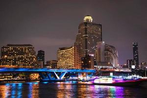 buntes nachtbild der asiatischen stadt - blaulichtbrücke über großen fluss und gebäudehintergrund in bangkok thailand foto