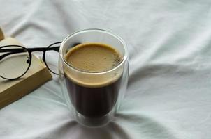 morgens ein glas heißen kaffee mit buch und brille auf dem bett. zu hause bleiben und entspannendes konzept. foto