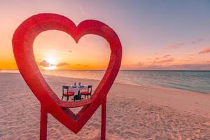 Abendessen für Flitterwochenpaare bei privatem, luxuriösem, romantischem Abendessen am tropischen Strand auf den Malediven. Meerblick, erstaunliche Inselküste mit roten herzförmigen Tischstühlen. romantisches Liebesziel
