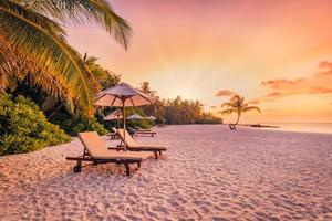 wunderschöne tropische Sonnenuntergangslandschaft, zwei Sonnenliegen, Liegestühle, Sonnenschirm unter Palmen. weißer Sand, Meerblick mit Horizont, bunter Dämmerungshimmel, Ruhe und Entspannung. inspirierendes Strandresorthotel foto