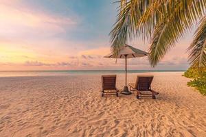 wunderschöne tropische Sonnenuntergangslandschaft, zwei Sonnenliegen, Liegestühle, Sonnenschirm unter Palmen. weißer Sand, Meerblick mit Horizont, bunter Dämmerungshimmel, Ruhe und Entspannung. inspirierendes Strandresorthotel foto