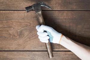 Hand, die Hammer auf Holztischhintergrund hält. foto