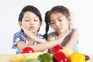 asiatische Jungen und Mädchen zeigen Abneigung Ausdruck mit frischem buntem Gemüse isoliert auf weißem Hintergrund foto