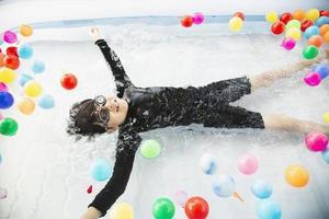 Junge, der mit buntem Ball im kleinen Swimmingpoolspielzeug spielt - fröhlicher Junge im Wasserpool-Spielzeugkonzept foto