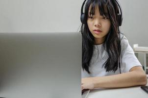 Mädchen mit Kopfhörern, die online mit einem Computer-Laptop lernen und entspannende Musik hören oder zu Hause soziale Medien im Internet spielen. foto