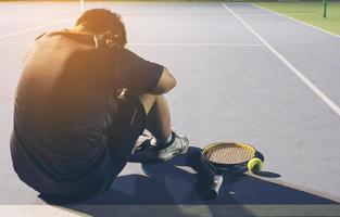 Trauriger Tennisspieler, der auf dem Platz sitzt, nachdem er ein Match verloren hat foto