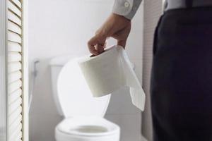 Mann sitzt auf Toilettenschüssel und hält Seidenpapier - Konzept für Gesundheitsprobleme foto