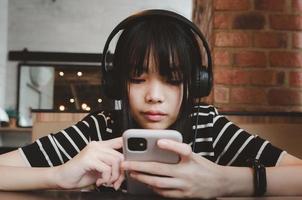 Teenager-Mädchen trägt Kopfhörer und hält ein Handy-Smartphone in den sozialen Medien, das sich auf dem Sofa entspannt. foto