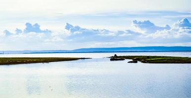 Seenlandschaft gibt es einen mit grünem Gras bedeckten Hügel. ein entfernter Berg nahe dem Horizont, wo sich tagsüber bei schlechtem Wetter schwarze Regenwolken bildeten foto