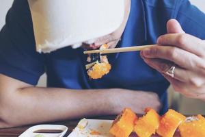 asiatischer mann, der maki-sushi isst foto