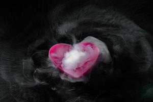 Rauch von Trockeneis mit rosa herzförmiger Tasse isoliert auf schwarzem Hintergrund foto
