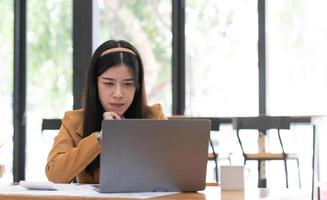 junge asiatische frau, die im büro arbeitet und einen laptop auf einem tisch verwendet. foto
