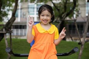 asiatisches glückliches mädchen mit orangefarbenem kleid spielt auf dem spielplatz. foto