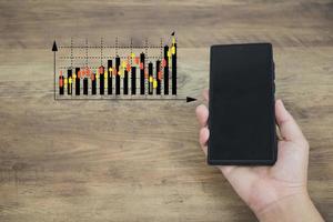 finanz- und investitionstechnologiekonzept männerhände sind aktives smartphone, um aktiendiagrammanalysen zu planen, um in finanzmärkte zu investieren. die andere Seite hat ein virtuelles Bild als Candlestick-Chart. foto