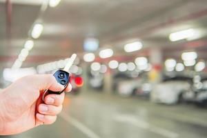 Eine Mannhand drückt die Auto-Fernbedienungstaste, um zu öffnen - schließen Sie sein Auto auf dem Parkplatz foto